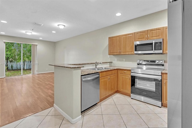 kitchen with light tile patterned flooring, sink, light stone counters, appliances with stainless steel finishes, and kitchen peninsula