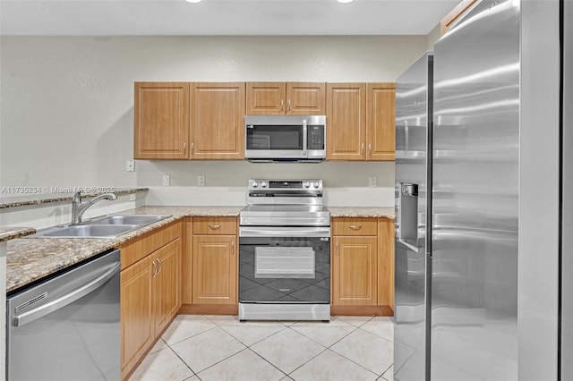 kitchen with appliances with stainless steel finishes, light stone countertops, sink, and light tile patterned floors