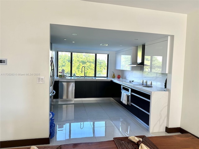 kitchen featuring sink, wall chimney range hood, stainless steel appliances, tile patterned flooring, and backsplash