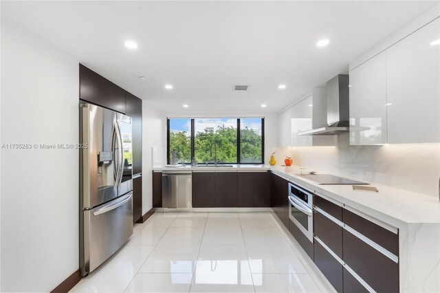 kitchen featuring tasteful backsplash, white cabinetry, light tile patterned floors, stainless steel appliances, and wall chimney range hood