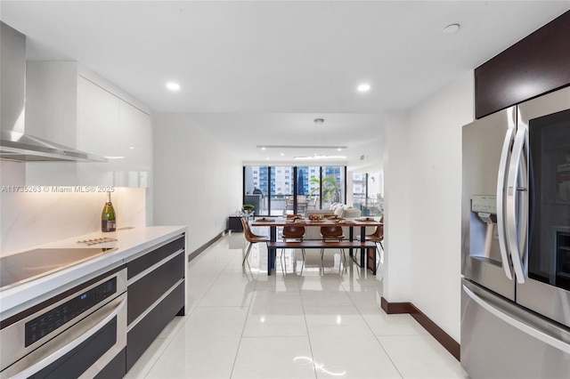 kitchen featuring pendant lighting, white cabinetry, light tile patterned floors, stainless steel appliances, and wall chimney range hood