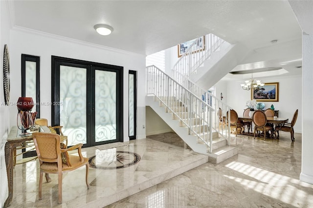 foyer with ornamental molding, a notable chandelier, and french doors