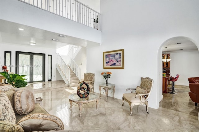 living room with a towering ceiling, ornamental molding, and french doors