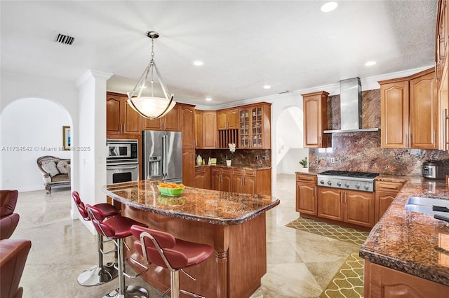 kitchen featuring a kitchen island, appliances with stainless steel finishes, pendant lighting, a breakfast bar, and wall chimney range hood