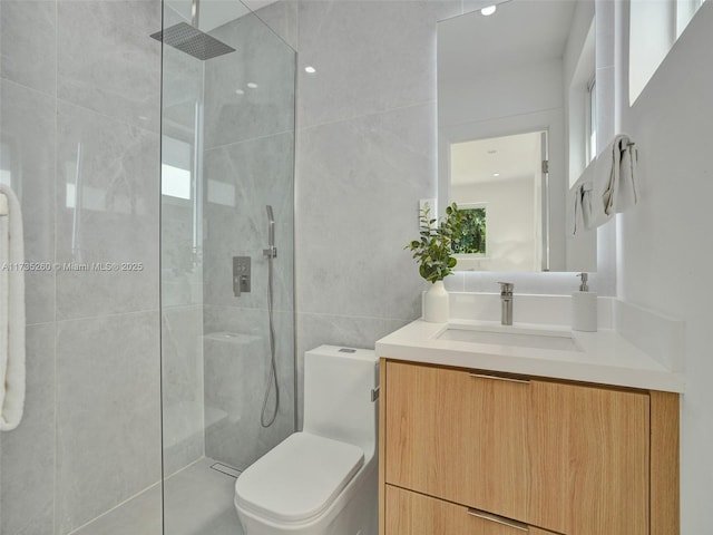 bathroom with vanity, a tile shower, tile walls, and toilet