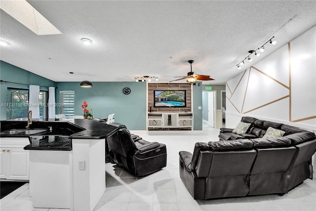 living room with a skylight, rail lighting, sink, ceiling fan, and a textured ceiling