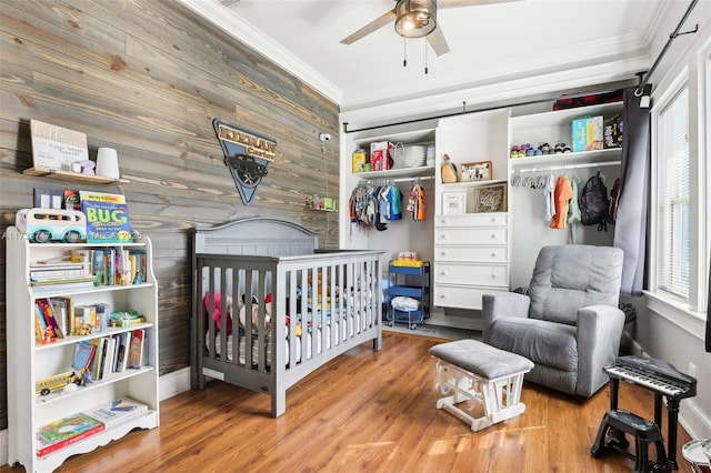 bedroom with hardwood / wood-style floors, wooden walls, ornamental molding, a crib, and a closet