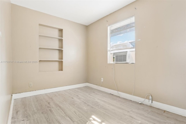 spare room featuring cooling unit, built in shelves, and light hardwood / wood-style flooring