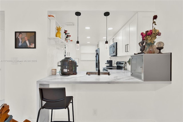 kitchen featuring decorative light fixtures, white cabinetry, light stone counters, kitchen peninsula, and stainless steel appliances