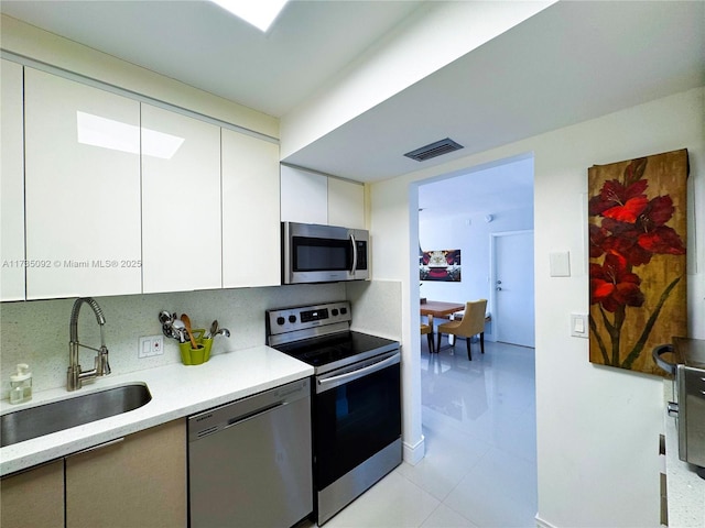 kitchen featuring sink, tasteful backsplash, white cabinetry, light tile patterned floors, and appliances with stainless steel finishes