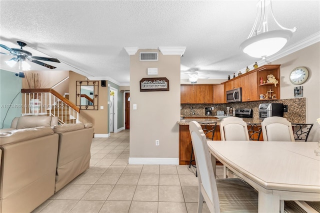 tiled dining area with ceiling fan, ornamental molding, and a textured ceiling