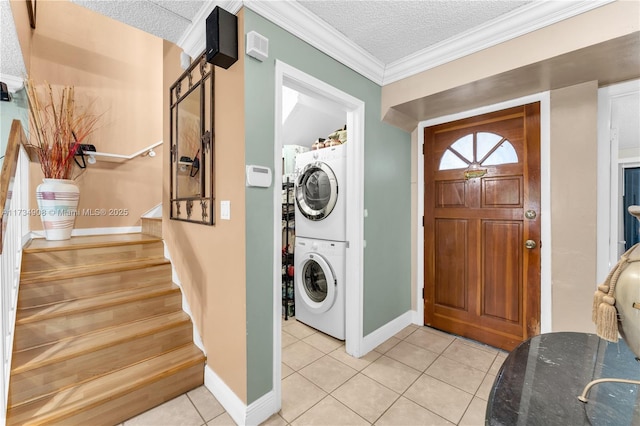 laundry area featuring light tile patterned floors, ornamental molding, stacked washer and clothes dryer, and a textured ceiling