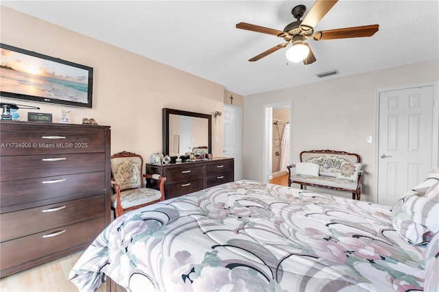 bedroom with ceiling fan, connected bathroom, a textured ceiling, and light wood-type flooring