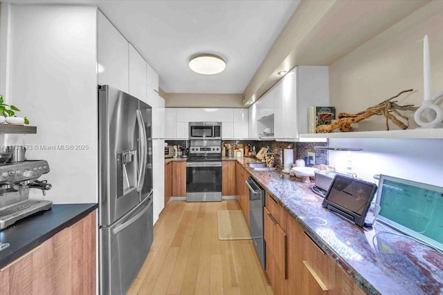 kitchen featuring appliances with stainless steel finishes, tasteful backsplash, white cabinetry, sink, and light hardwood / wood-style floors