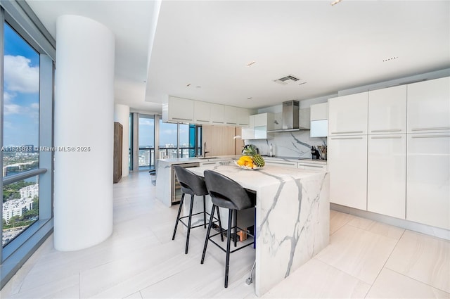 kitchen featuring wall chimney exhaust hood, a breakfast bar area, white cabinetry, tasteful backsplash, and a center island