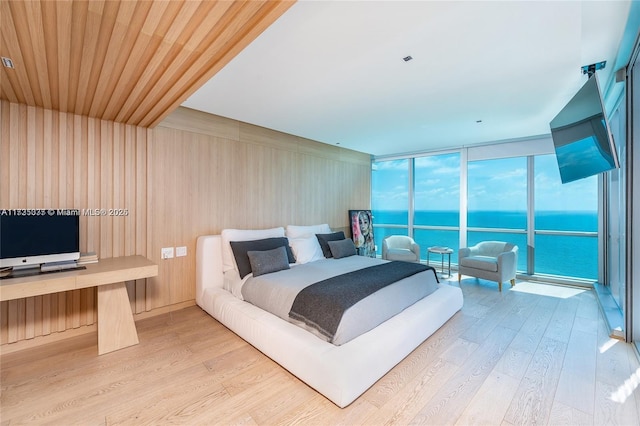 bedroom with a wall of windows, wooden ceiling, and light wood-type flooring