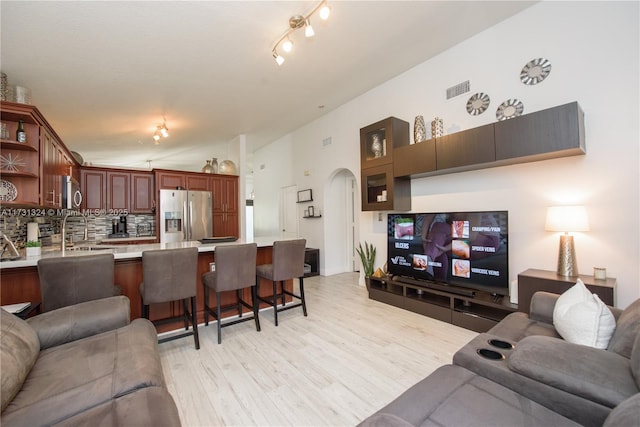 living room with lofted ceiling, sink, and light hardwood / wood-style flooring