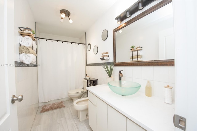 bathroom with wood-type flooring, tile walls, vanity, toilet, and a bidet