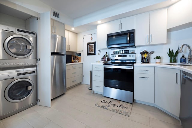 kitchen featuring white cabinets, stainless steel appliances, sink, and stacked washer and clothes dryer