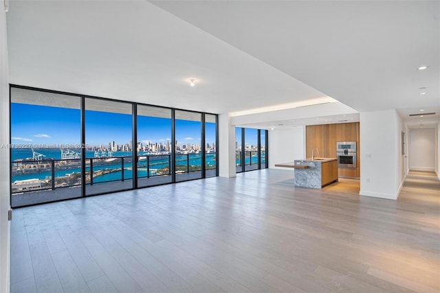 unfurnished living room with a water view, sink, a wall of windows, and light hardwood / wood-style floors