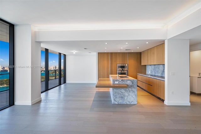 kitchen featuring an island with sink, sink, backsplash, light hardwood / wood-style floors, and floor to ceiling windows