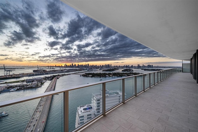 balcony at dusk featuring a water view