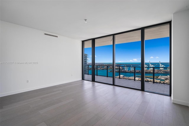 unfurnished room featuring a water view, a wall of windows, and hardwood / wood-style flooring