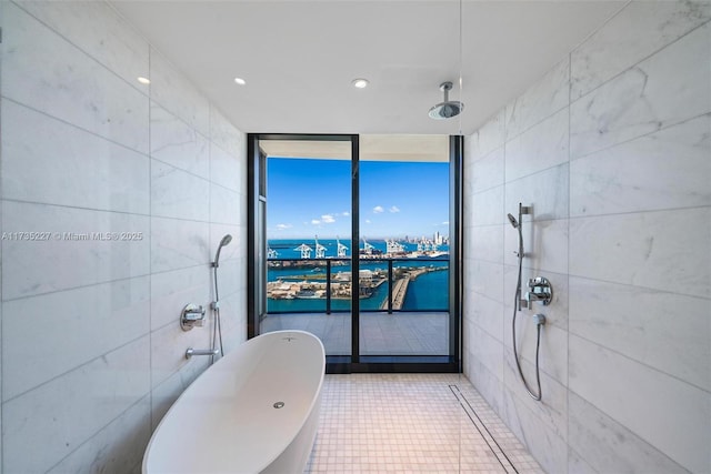 bathroom with tile walls, tile patterned flooring, a water view, expansive windows, and a bathing tub