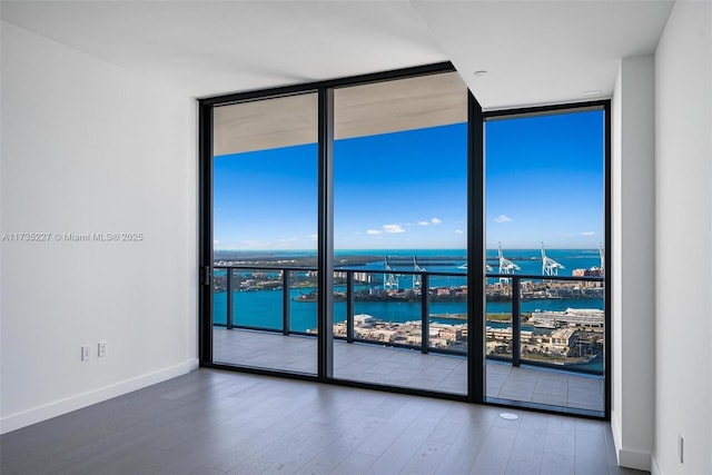 empty room featuring wood-type flooring, a water view, and a wall of windows