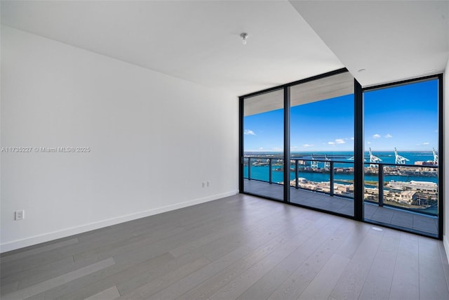 unfurnished room with expansive windows, a water view, and hardwood / wood-style floors