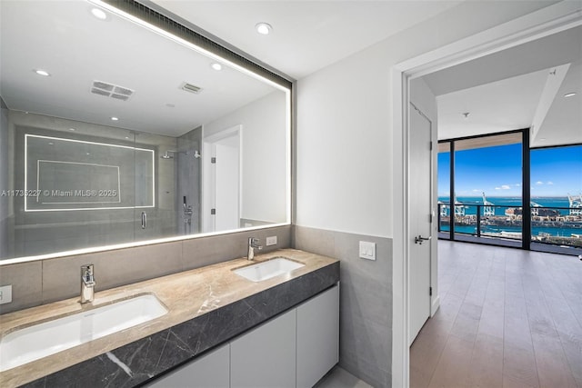 bathroom featuring walk in shower, tile walls, vanity, expansive windows, and hardwood / wood-style floors