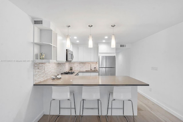 kitchen featuring stainless steel appliances, kitchen peninsula, a breakfast bar area, and white cabinets