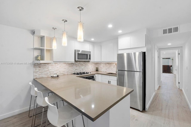 kitchen featuring white cabinetry, a kitchen breakfast bar, hanging light fixtures, kitchen peninsula, and stainless steel appliances