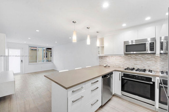 kitchen featuring white cabinetry, appliances with stainless steel finishes, decorative light fixtures, and kitchen peninsula