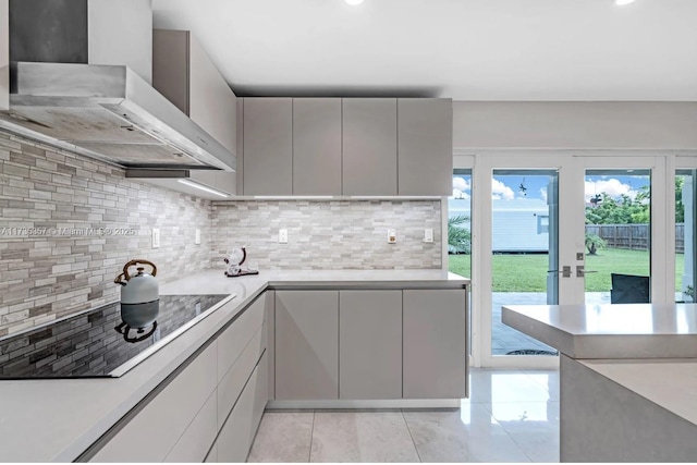 kitchen featuring black electric stovetop, wall chimney range hood, and decorative backsplash