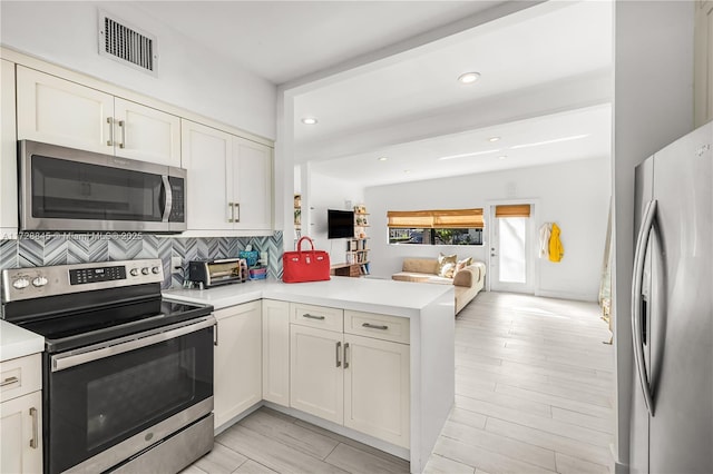 kitchen with white cabinetry, light wood-type flooring, kitchen peninsula, stainless steel appliances, and decorative backsplash