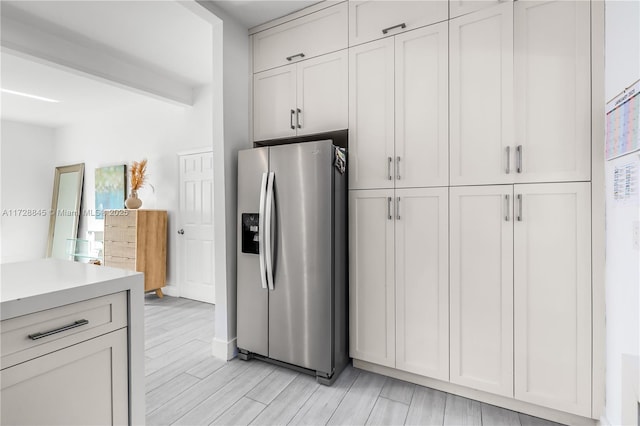 kitchen featuring stainless steel fridge, beam ceiling, wood tiled floor, and light countertops