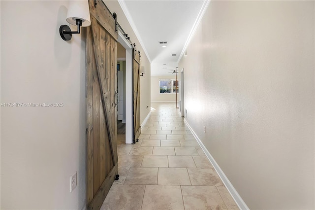 corridor featuring light tile patterned floors, crown molding, and a barn door