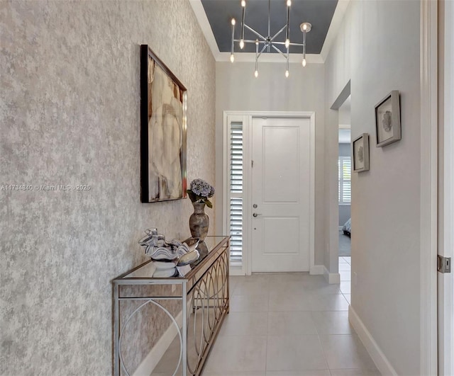 hall featuring tile patterned floors, baseboards, a chandelier, and crown molding