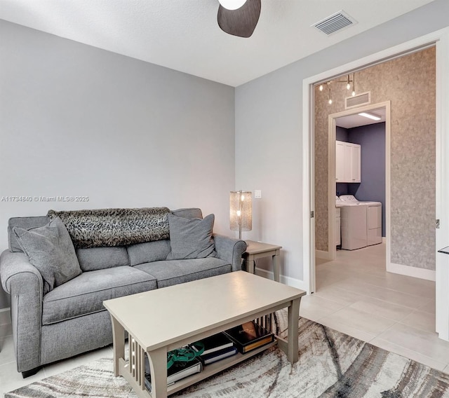 living room featuring separate washer and dryer, ceiling fan, baseboards, and light tile patterned floors