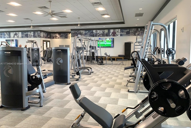 exercise room featuring a tray ceiling, light colored carpet, and ceiling fan