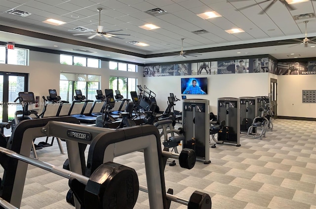 gym with light colored carpet, a ceiling fan, plenty of natural light, and a tray ceiling
