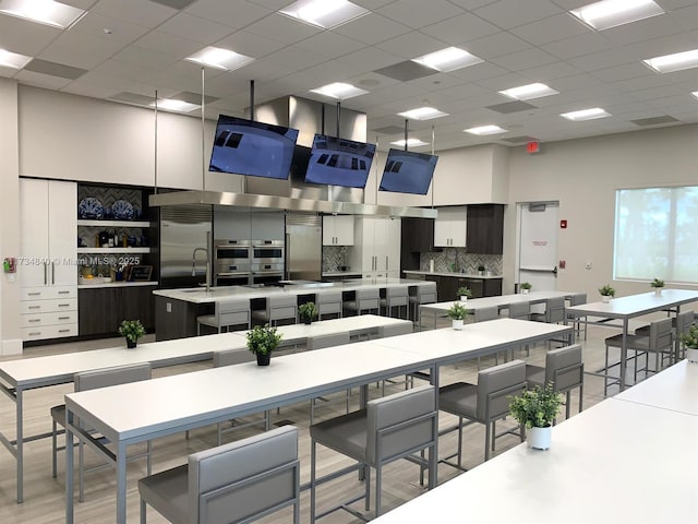 kitchen with tasteful backsplash, white cabinetry, a towering ceiling, and an island with sink