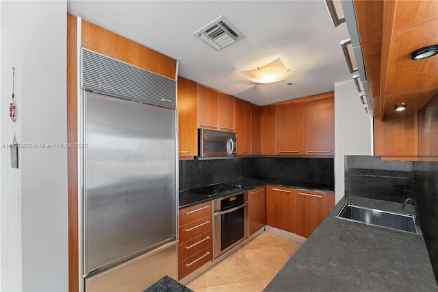 kitchen with appliances with stainless steel finishes, tasteful backsplash, sink, dark stone countertops, and light tile patterned floors