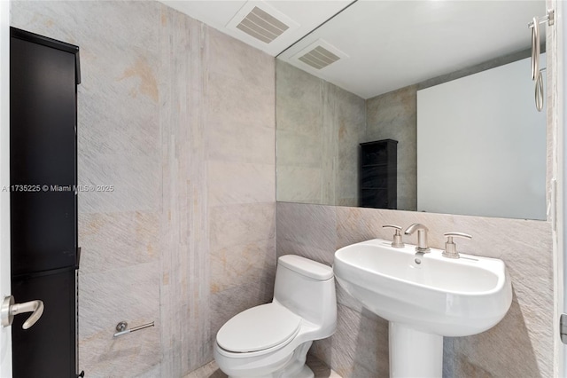 bathroom with toilet, sink, and tile walls