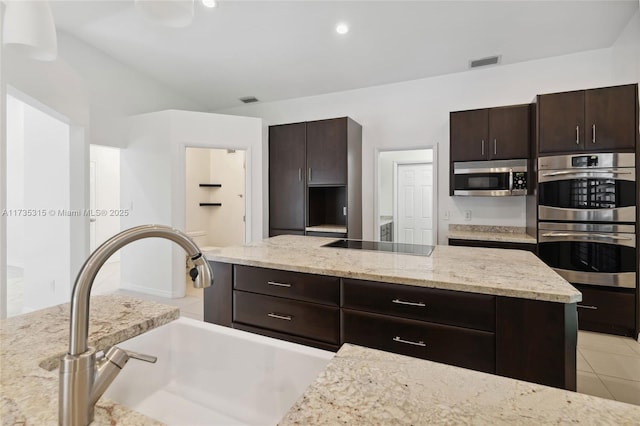 kitchen with sink, light tile patterned floors, appliances with stainless steel finishes, dark brown cabinetry, and light stone countertops