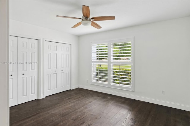 unfurnished bedroom with ceiling fan, two closets, and dark hardwood / wood-style flooring