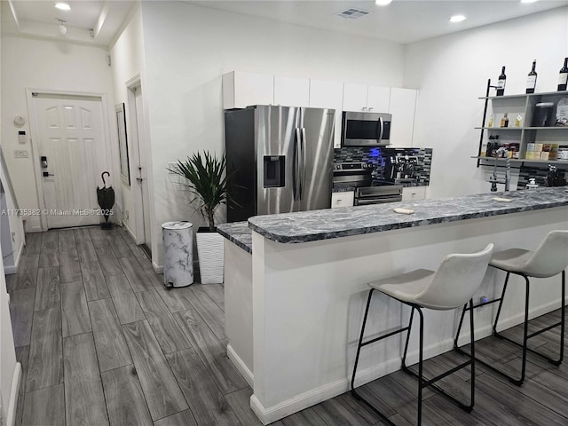 kitchen featuring tasteful backsplash, white cabinets, a kitchen breakfast bar, kitchen peninsula, and stainless steel appliances