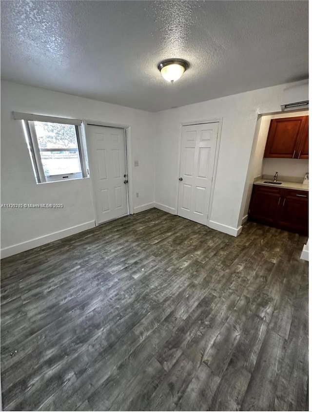 interior space with a textured ceiling, a wall mounted AC, dark wood finished floors, and baseboards