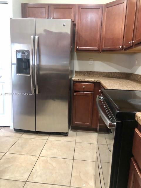 kitchen featuring light tile patterned floors, stainless steel fridge, and black / electric stove